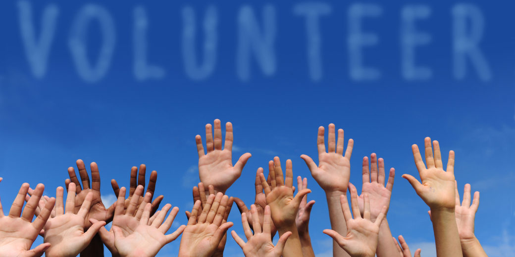 volunteer group raising hands against blue sky background